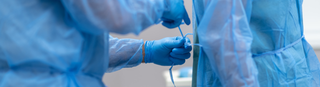 Medical worker ties a blue medical gown onto another worker.