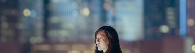 Woman outside on rooftop alone with cityscape in the background.