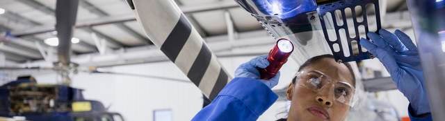 Female helicopter mechanic examining part with flashlight