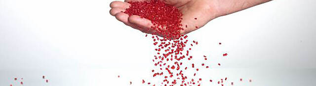 A hand catching red plastic pellets