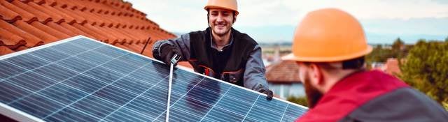 Two technicians install a solar planel on a tile rooftop