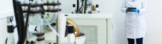 A scientist types on a tablet during CBDa oil extraction. She stands next to a rotational vaporizer.