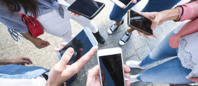 A group of young adults scrolling through their cell phones. 