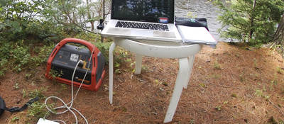 Portable power pack connected to laptop in a nature scene.