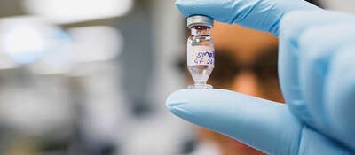 Gloved hand holding a chemical vial in a laboratory setting
