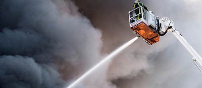 Firefighter on aerial ladder spraying hose against smoky sky