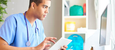 A medical professional reading a chart on a tablet and desktop monitor