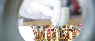 A close-up image of a gloved hand connecting wires in a laboratory setting. 