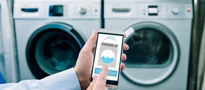 A man using his phone thats connected to a washing machine