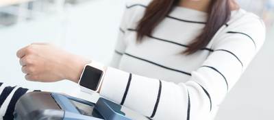 A woman holds her smartwatch up to a grey scanner