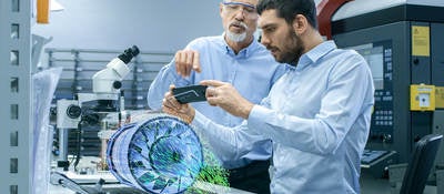 Two Engineers Works with Mobile Phone Using Augmented Reality Holographic Projection 3D Model of the Engine Turbine Prototype