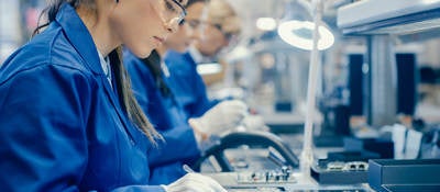 Female electronics factory workers in protective glasses assembling printed circuit boards 