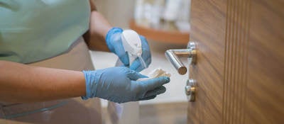 Employee spraying disinfectant on cloth to sanitize door handle