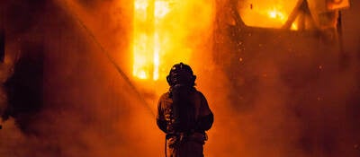 A firefighter sprays water on the outside of a burning building