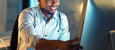 Smiling man sitting at a desk in front of a computer monitor