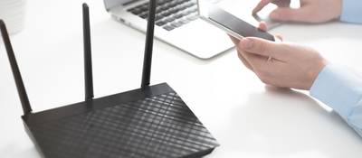 Wireless router positioned next to a laptop and mobile phone on a white table.