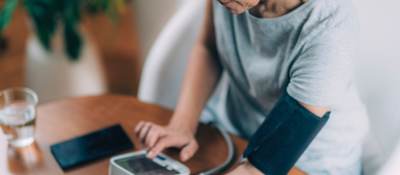 Woman measuring blood pressure and checking parameters via smartphone