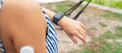 Young woman with wearable patch on arm checking a smartwatch to see her blood sugar level.