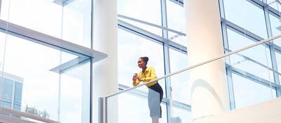 A Black woman looks down from the second floor of an interior office building.