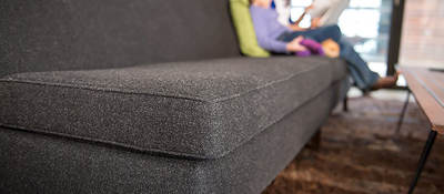 Woman and child comfortably sitting on a gray sofa, reading a book together