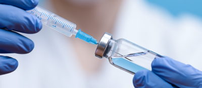 Gloved hand holding a vaccine vial and syringe