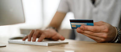 man typing on keyboard and holding a credit card for online payment