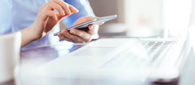 woman using a mobile phone in front of a laptop computer