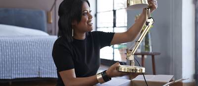 Young woman opening box with lamp at home