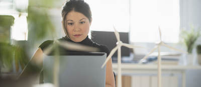 Person sitting at a desk using a laptop with miniature wind turbines sitting on the desk