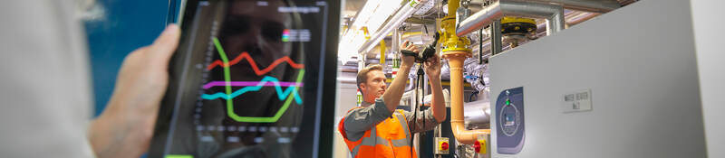 Chart on an iPad in foreground with a man adjusting pipes in the background
