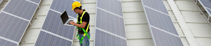 Man in safety gear inspecting solar farm with a laptop