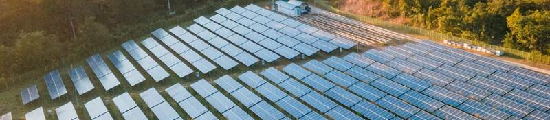 solar panels in open field surrounded my trees and mountains in the distance