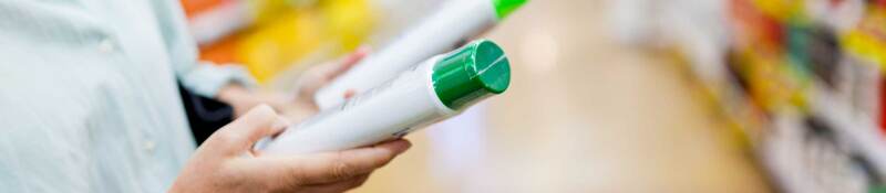 Person comparing green and white plastic bottles in a supermarket