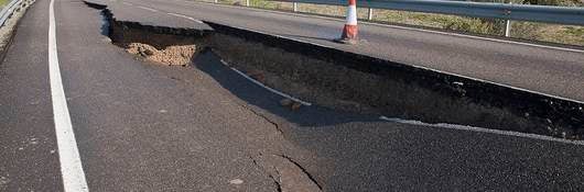 A two-lane road with a giant hole, caused by a landslide, in the middle of the road.