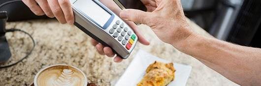 cropped image of customer paying through mobile phone over electronic reader at cafe counter