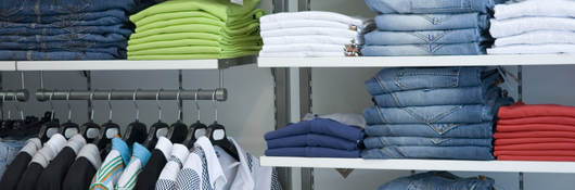 Retail store shelves filled with neatly folded clothes arranged by color. 