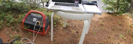 Portable power pack connected to laptop in a nature scene.
