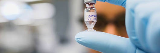 Gloved hand holding a chemical vial in a laboratory setting