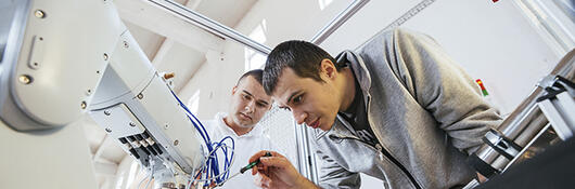 Two men work on robot.