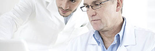 Two men in lab coats looking at a laptop. 