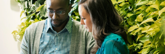 man and woman sitting next to one another in front of foliage