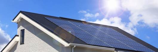 The sun shines brightly on the solar panels installed on the roof of a white, stucco home.