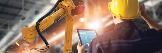 engineer in factory with tablet looking at robot arm