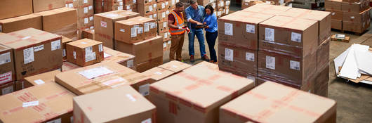 A few people in a warehouse surrounded in boxes.