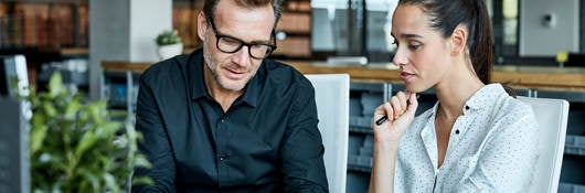 man and woman sitting next to one another at table looking at a tablet