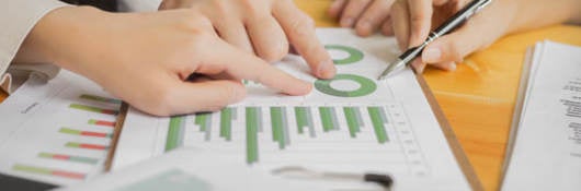 Close up of hands w/pen & pointing to a paper with graph on it