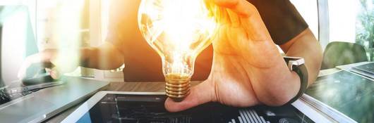 A man in a burgundy shirt holds a light bulb in his left hand, which is placed over a smart pad.