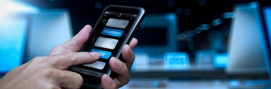 A hand holds a smartphone while the other hand converses with a chatbot.