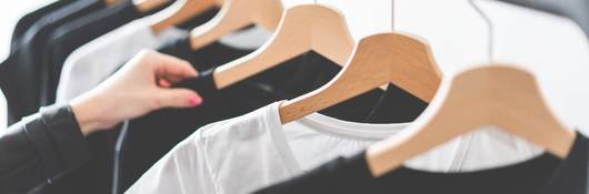A customer browses black and white t-shirts hanging on steel retail rack.