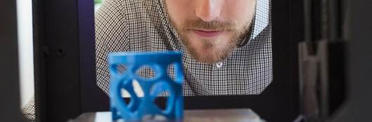 Man looks at a blue gadget made with additive manufacturing